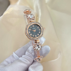 Detail of rose gold ladies watch with rhinestone strap and dark grey dial held by hand