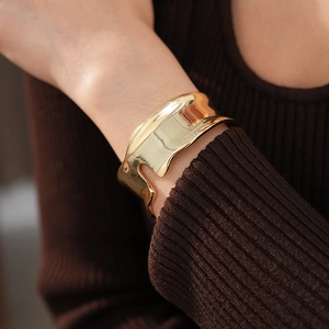 Primo piano di un ampio bracciale rigido dorato irregolare al polso di una donna