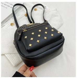 Detail of a black mini backpack with gold square rivets and metallic zipper on a fabric background