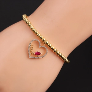 Bracelet à billes dorées avec pendentif cœur, cristal rouge et gravure LOVE sur poignet