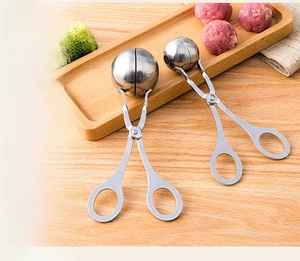 Dual stainless steel meatball makers in different sizes on a wooden tray with fresh food