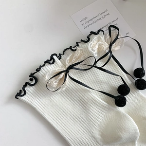 Close-up of white ribbed socks with black ruffle trim and lace bow with pom-pom ties