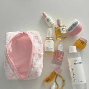 Overhead view of pink bow cosmetic bag with skincare products on white background