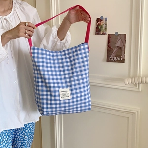 Détail du cabas en toile à carreaux bleus avec bandoulière rose et étiquette tissée