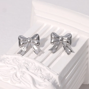 Minimalist silver bow knot stud earrings in stainless steel on white textured base