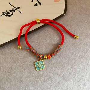 Détail du bracelet en soie tressée rouge avec pendentif Fu doré et éventail calligraphié
