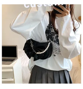 Detailed view of black bow shoulder bag featuring elegant white pearl strap and metal chain