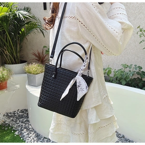 Detail of black woven bucket bag with elegant floral silk scarf handle and long strap