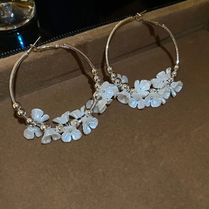 Macro view of large silver hoops featuring white acrylic flowers with metallic bead centers