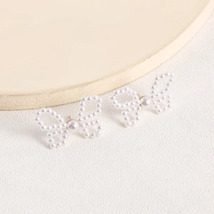 Detail of handcrafted butterfly earrings featuring imitation pearls on a textured background