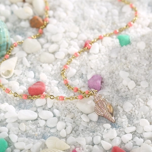 Detail of gold chain necklace with pink beads and conch shell pendant on white sand