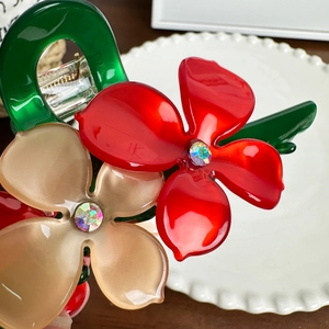 Green acetate flower hair claw clip with red rhinestones on a wooden table