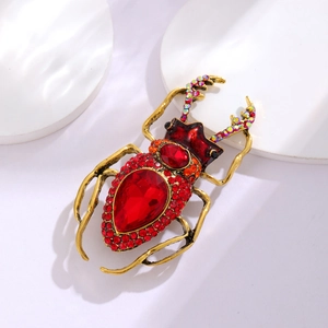 Macro shot of gold beetle brooch featuring a large red gemstone and sparkling rhinestones