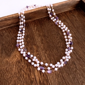 Close-up of triple-layered pearl and amethyst beaded necklace on a dark wooden tray