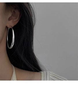 Vue latérale d'une grande boucle d'oreille créole géométrique argentée sur modèle