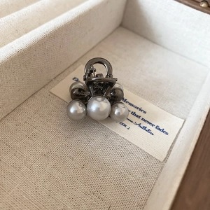 Macro detail of mini pearl hair claw clip with gunmetal finish on a display card