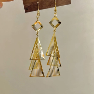 Détail de boucles d'oreilles dorées avec triangles superposés et paillettes métalliques