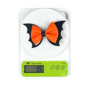Detail shot of a 9.6g Halloween bat bow hair clip on a scale showing light weight