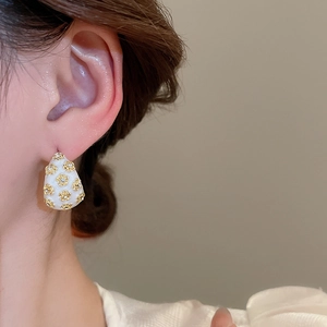 Detail of a white drop-shaped C-style earring featuring a gold flower with a small crystal
