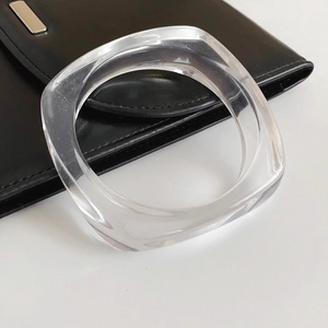 Nahaufnahme eines transparenten Harz-Armreifs auf einer schwarzen Ledertasche vor Weiß