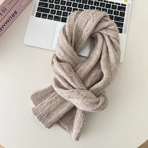 Detailed flat lay of a chunky knit wool scarf in soft beige on a minimalist desk