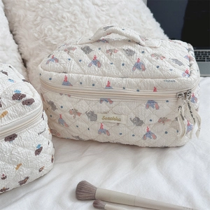 Close-up of beige quilted makeup bags featuring blue elephant pattern with top handle