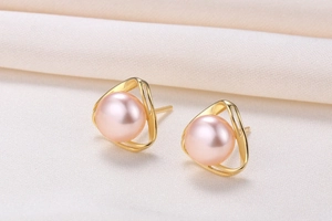 Detailed macro view of pink freshwater pearls on gold triangle studs on beige fabric