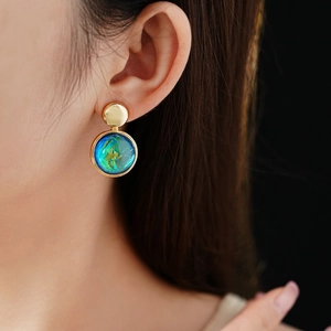 Close-up of elegant turquoise resin earrings with golden metal rims on a female model