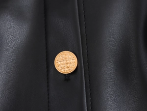 Close-up of golden textured buttons and stitching on black biker style faux leather dress