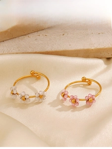 Close-up of gold-plated rings with white and pink beaded flowers on silk fabric