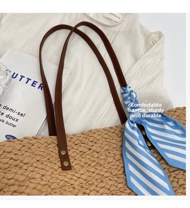 Detail of straw woven tote bag featuring brown leather handles and a blue striped scarf