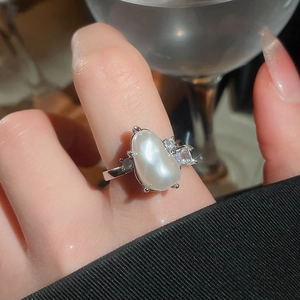 Detailed view of an irregular white pearl ring with zircon accents on a finger