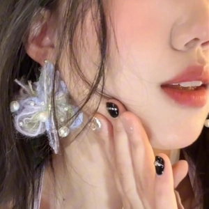 Close-up of oversized plush flower earrings with pearls and crystals on a model