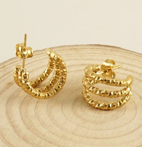 Close-up of gold-plated U-shaped earrings with triple-layered texture on wood