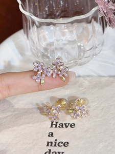 Macro shot of purple enamel flower stud earrings with a gold base held on a finger