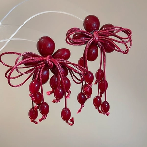 Detail of deep red beaded tassel earrings with woven bow design on a macro display