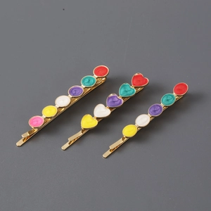 Detailed view of three gold-tone metal hair clips with colorful enamel heart patterns