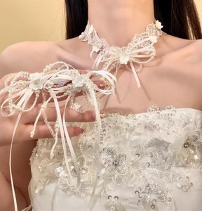 Dettaglio ravvicinato di un girocollo da sposa in pizzo bianco con fiocchi e perle.
