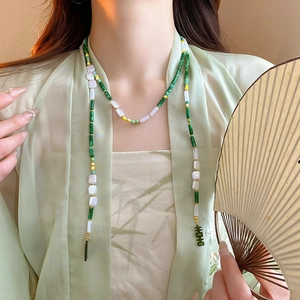 Detailed view of emerald beads and gold pendant on a neo-Chinese style long necklace