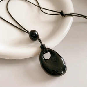 Close-up of a teardrop-shaped black glass pendant on a wax cord necklace