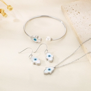 Detailed set of silver Hamsa jewelry with white shell and blue eye charms on a stone