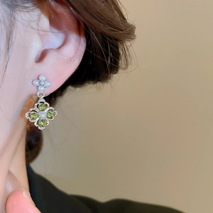 Close-up of floral pearl stud and diamond pendant earring with green crystals