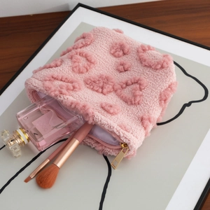 Close-up of pink plush makeup bag featuring heart texture and gold metal zipper