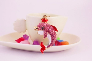 Detail of pink crystal dolphin pendant with red crown on a white decorative tray