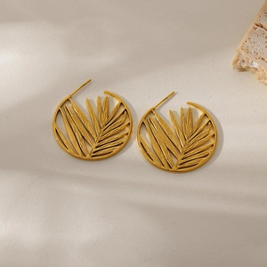 Golden round hollow tropical leaf drop earrings made of stainless steel on minimalist background
