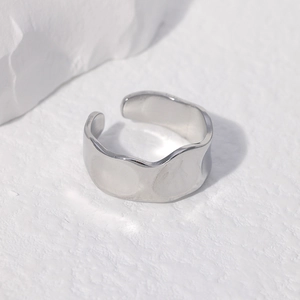 Close-up of polished silver irregular wave ring on minimalist white stone background