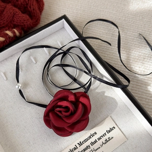 Detail of red fabric rose choker with black ribbon and a white pearl accent on a tray