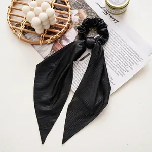 Detail of black pleated satin scrunchie with long ribbons on an aesthetic magazine layout