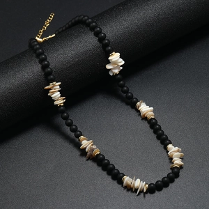 Collier bohème avec perles noires mates et fragments de coquillages sur support noir élégant