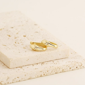 Close-up of gold snake hoop earrings with diamond accents on minimalist beige stones